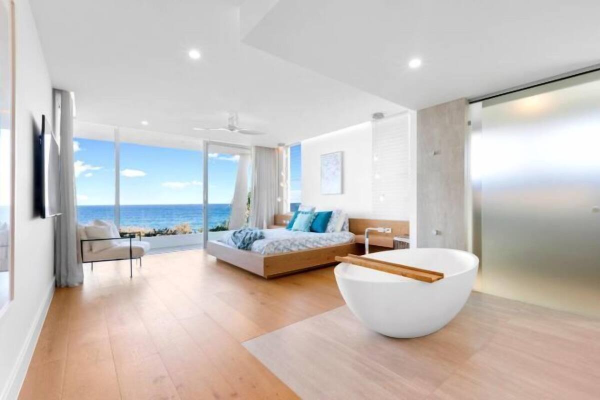 Een moderne slaapkamer met een groot bed, een wit bad en uitzicht op de oceaan.