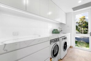 A modern kitchen with white cabinetry, a built-in washing machine, and a view of the outdoors. - Luxico Beaches at Sunrise (Heated Pool) (Sunrise Beach)