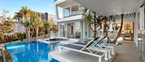 Una casa moderna con piscina, sillas de descanso y comedor.