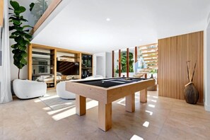 A modern indoor pool table in a well-lit room with a large plant, a wooden partition, and a view of a balcony. - Luxico Beaches at Sunrise (Heated Pool) (Sunrise Beach)