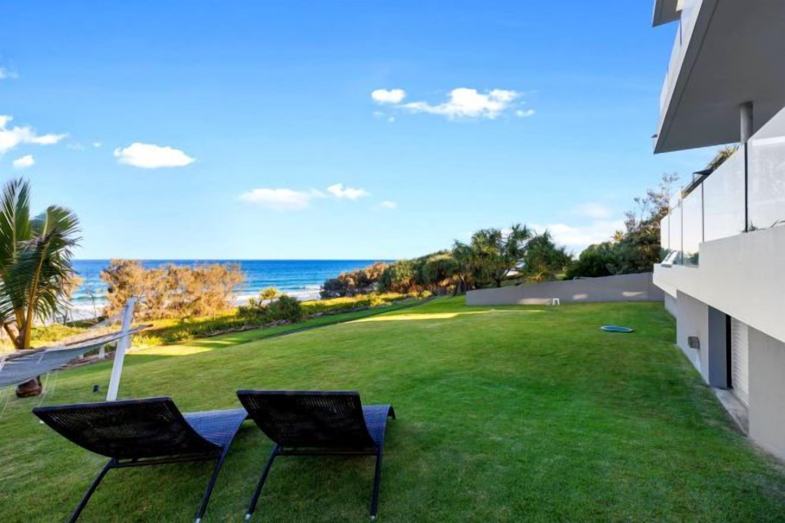 A grassy outdoor area with two lounge chairs facing a view of the ocean.