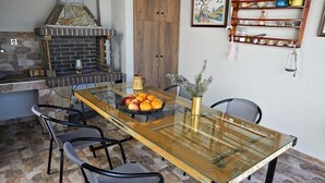 Een eetgedeelte met een glazen tafel, stoelen, een stenen open haard en een plank met servies.