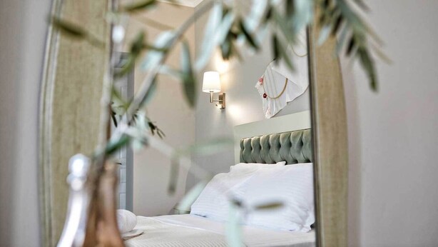 Een slaapkamer met een bed, een nachtkastje, een wandlamp en een spiegel die de kamer weerkaatst.