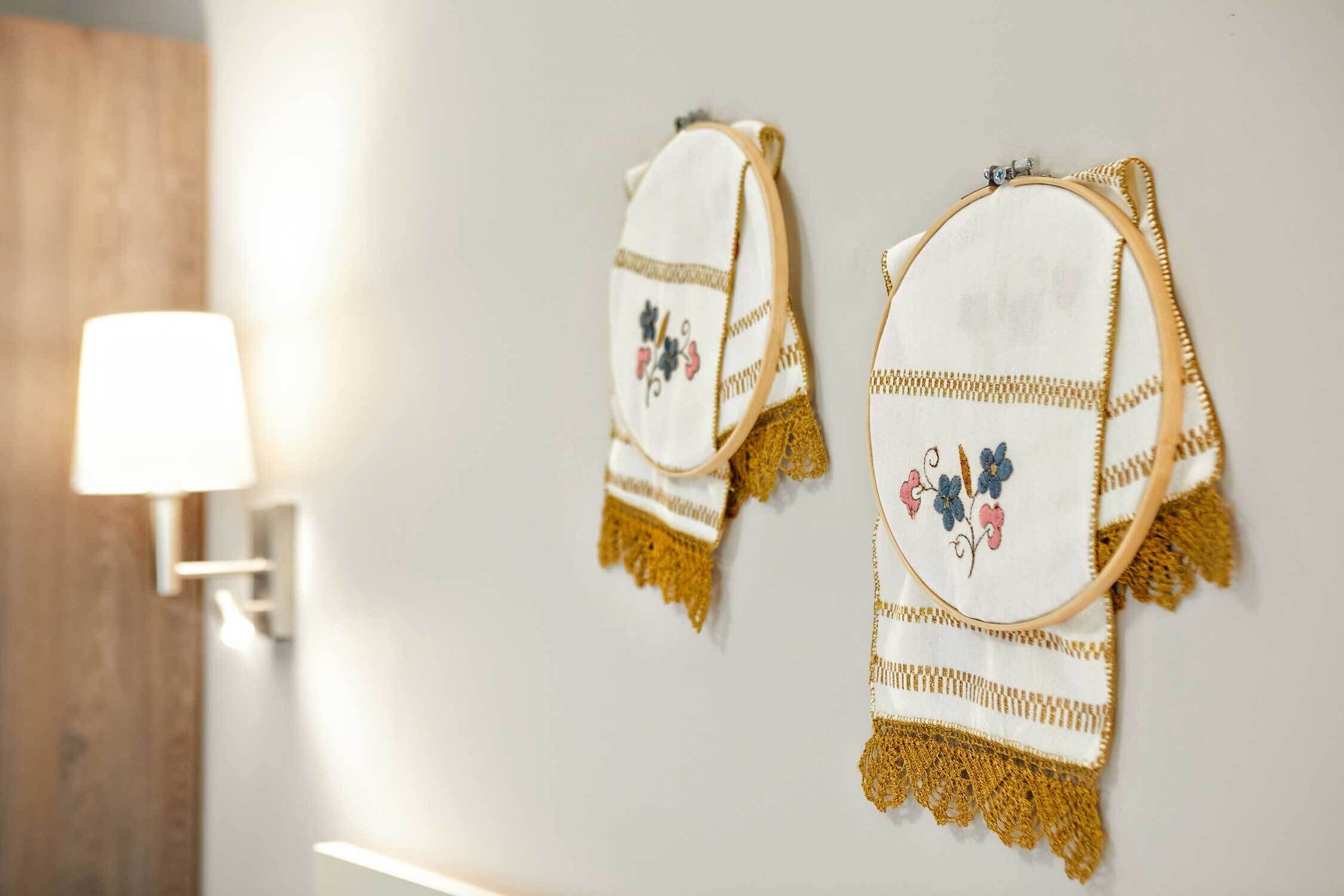 Dos toallas bordadas con flecos en una pared, una lámpara de pared y un panel de madera.