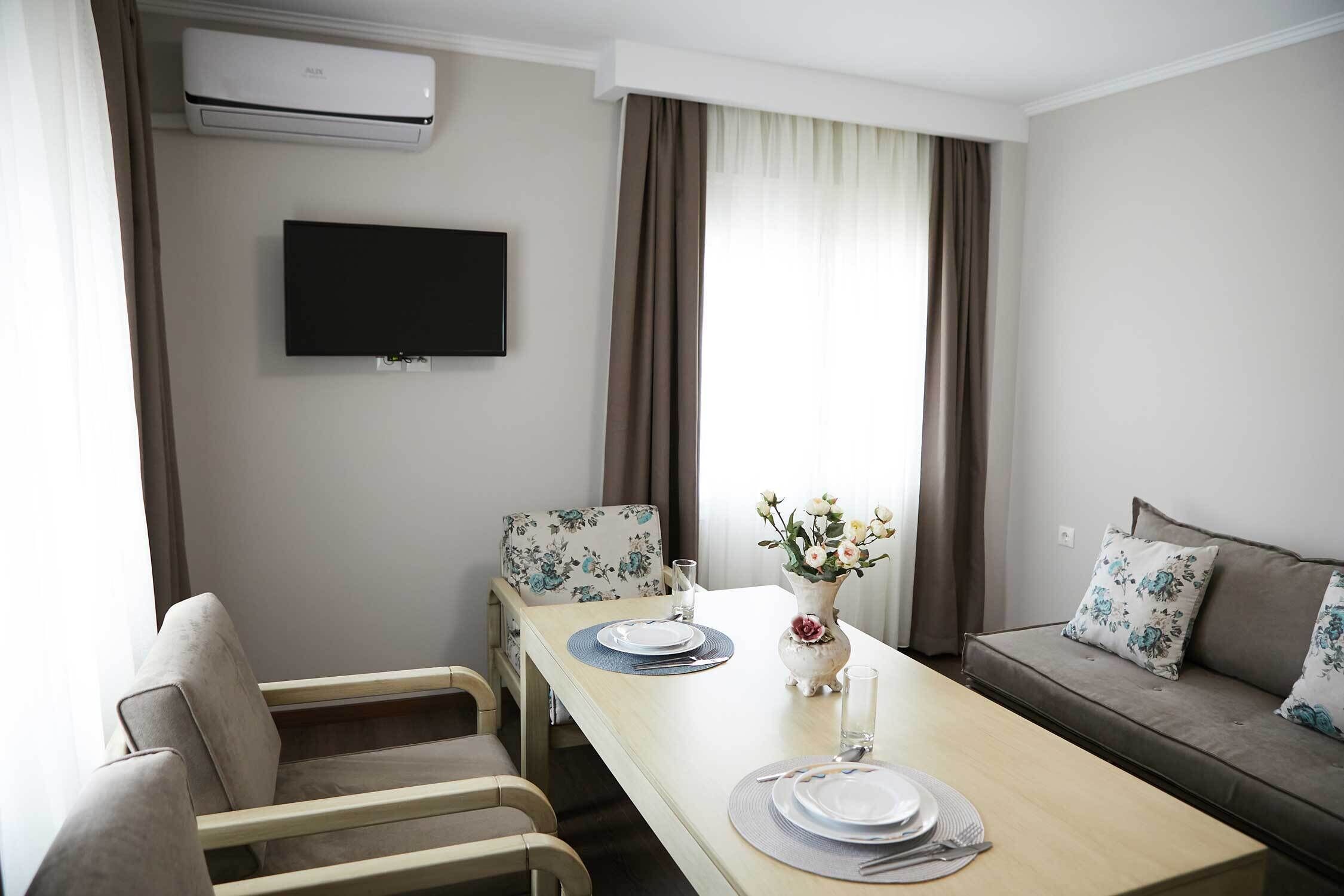 Een moderne woonkamer met een eettafel voor twee personen, een bank, een flatscreen televisie en een airconditioning.