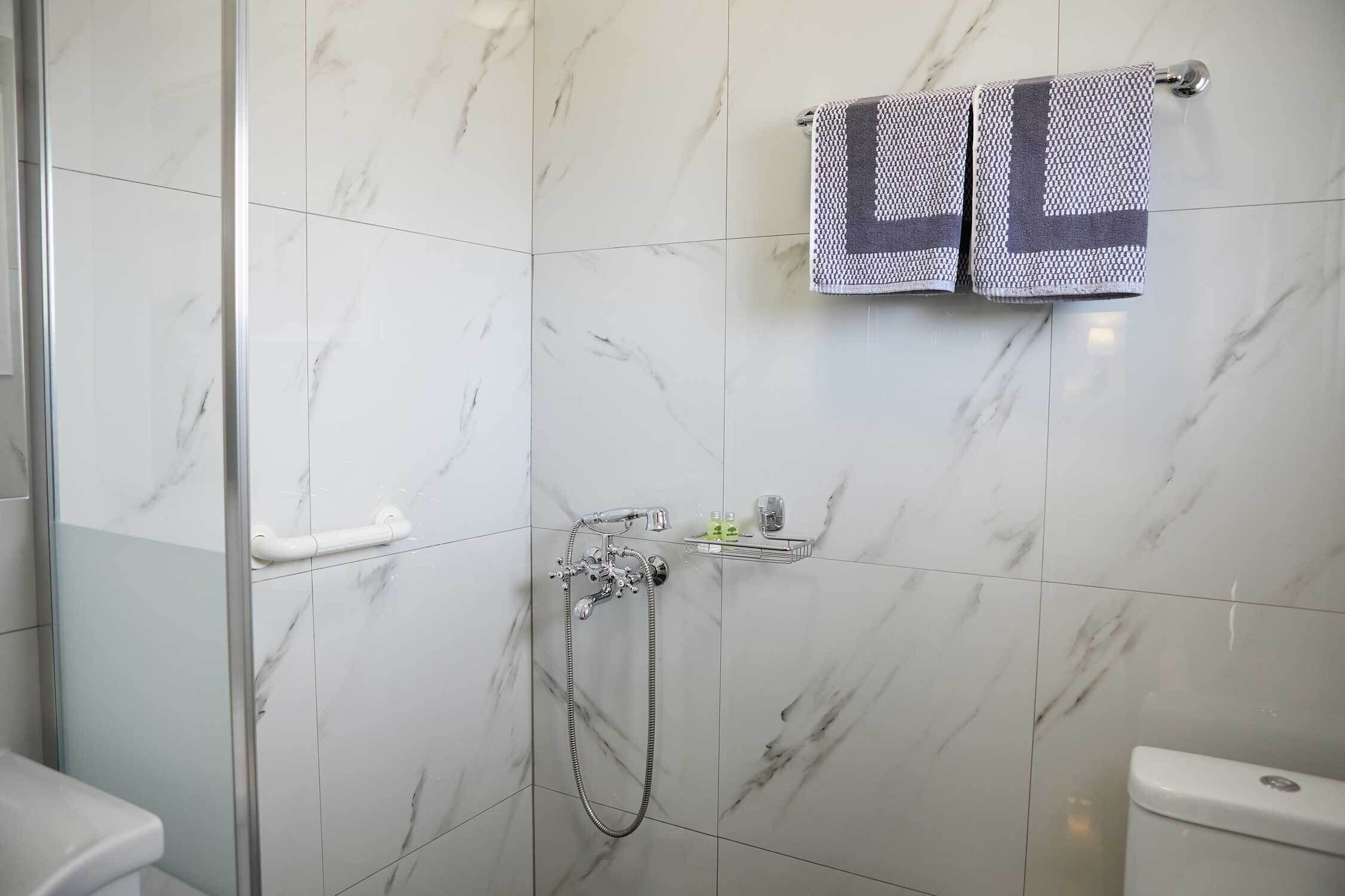 A bathroom with a glass shower enclosure, a toilet, and two towels hanging on a rack.