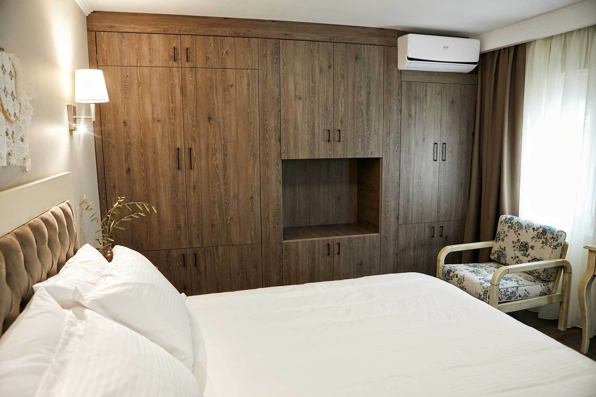 Une chambre d’hôtel avec un grand lit, une armoire en bois, un petit coin salon et un climatiseur fixé au mur.