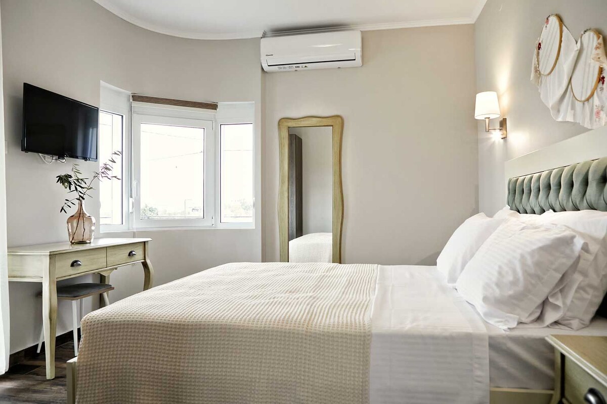Ein Hotelzimmer mit Bett, Nachttisch, Spiegel, an der Wand montiertem Fernseher und einem Fenster.