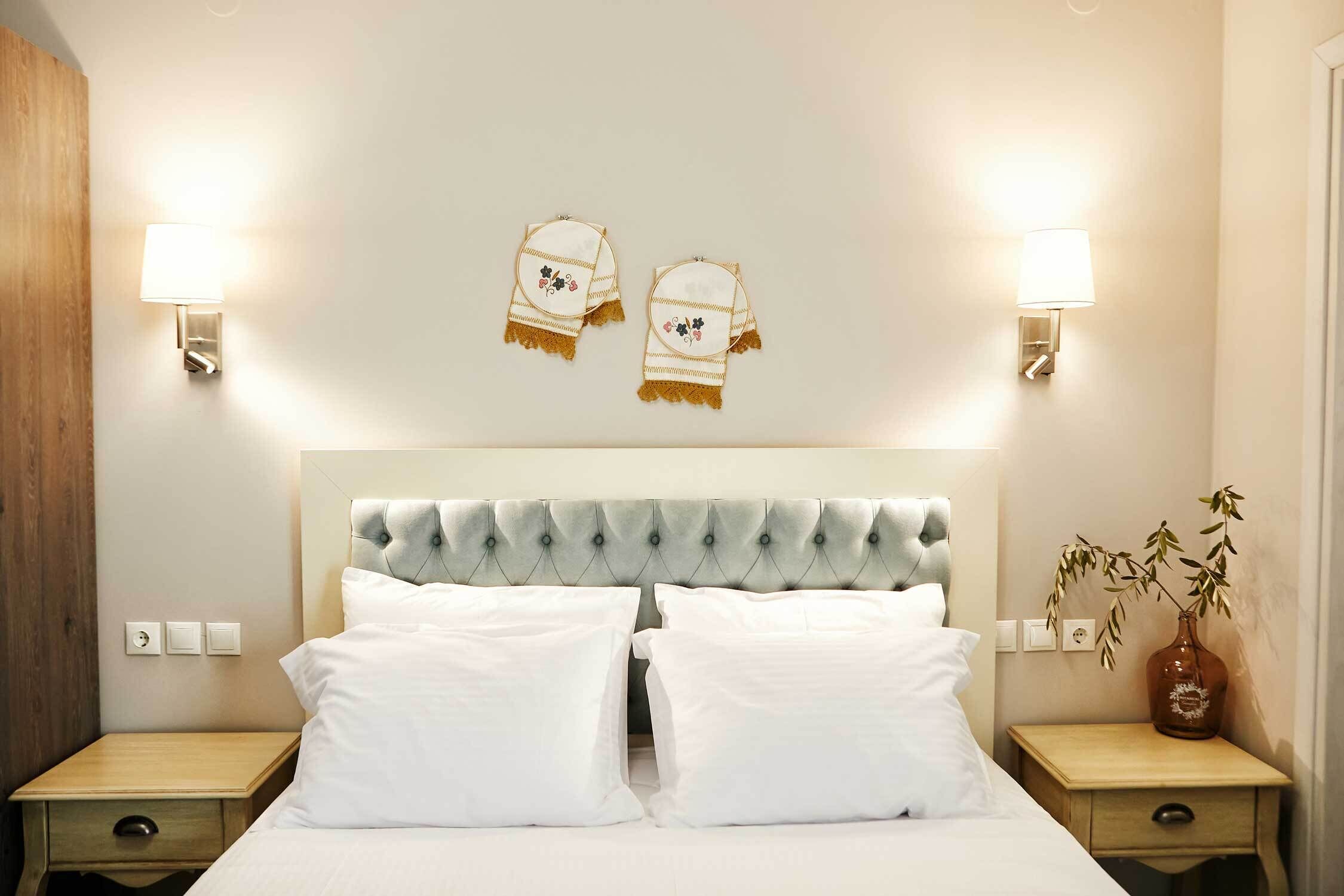 Hotellihuone, jossa on napitettulla päällistyksellä varustettu sängynpääty, kaksi yöpöytää, yölamppu ja seinään kiinnitetty valaisin.