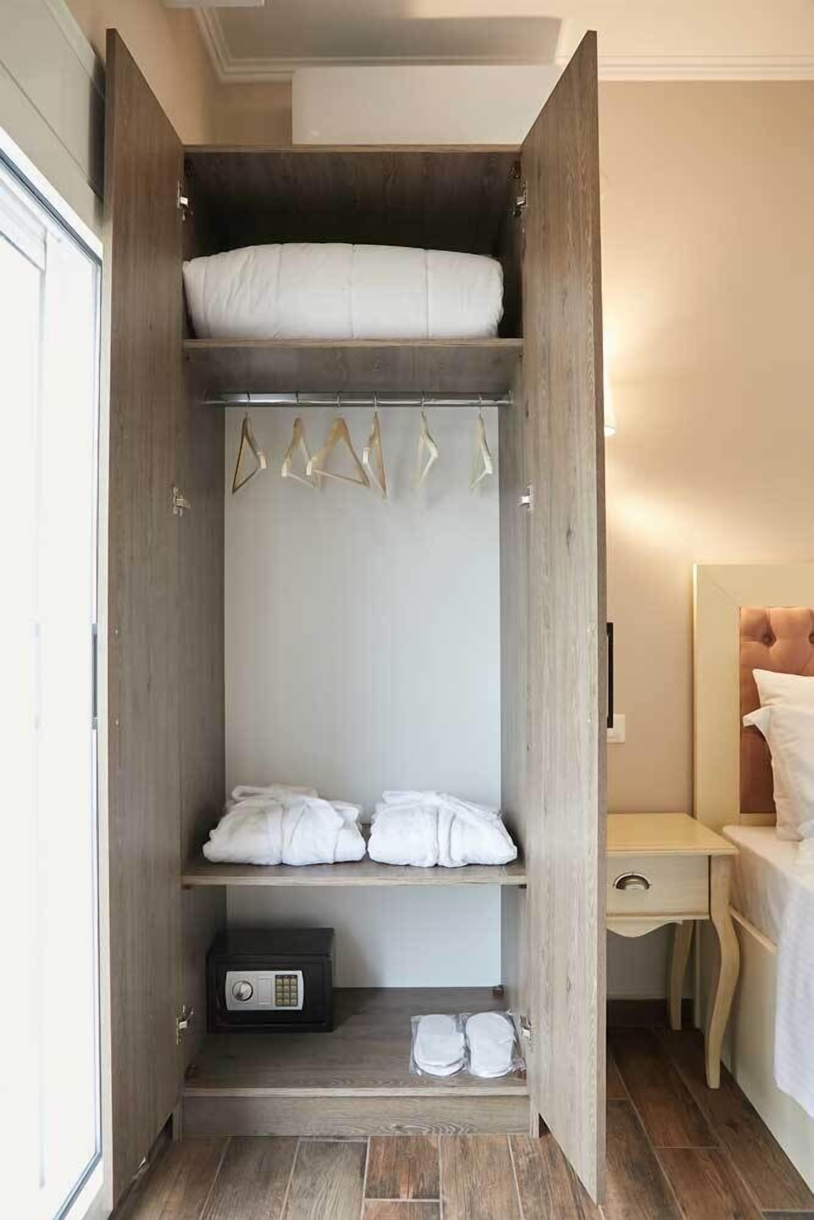 A walk-in closet with a bed at the end, shelves with folded towels, and a black electronic device on the bottom shelf.