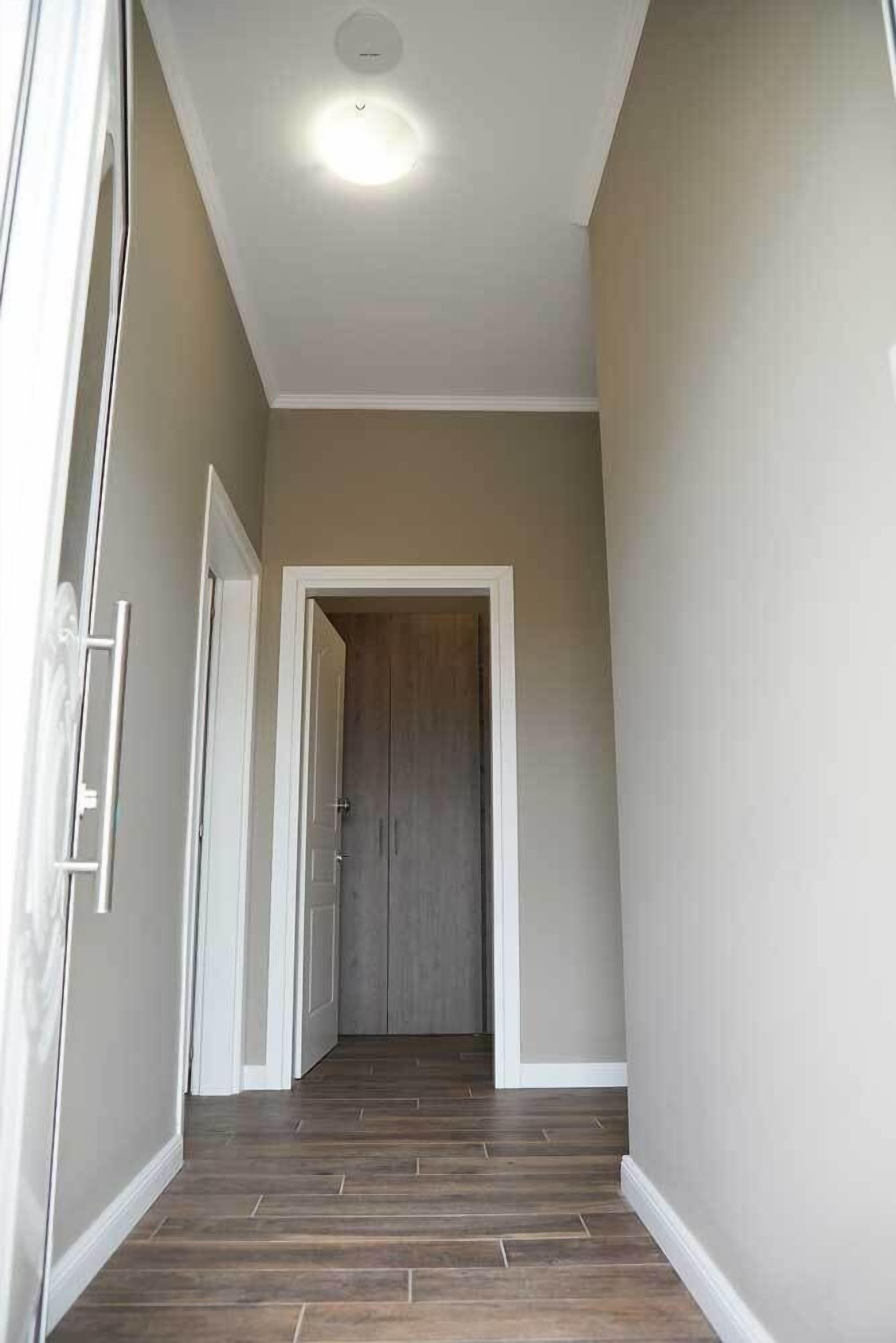 Un couloir avec un plancher en bois, des murs blancs et une porte au fond.