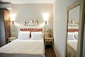 Une chambre à coucher bien aménagée, avec une tête de lit capitonnée, deux tables de chevet dotées de lampes et un miroir qui reflète la pièce.