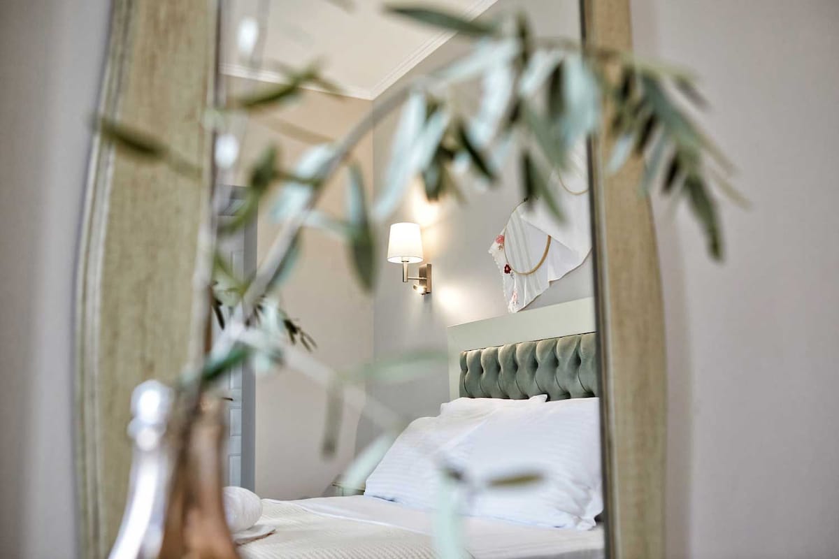Een slaapkamer met een bed, een nachtkastje, een wandlamp en een spiegel die de kamer weerkaatst.