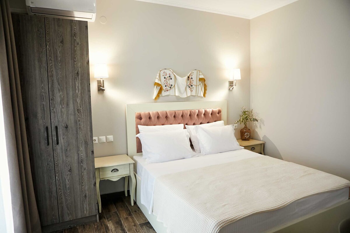 Un dormitorio con cabecera capitonada, una cama grande con ropa blanca, un armario de madera, lámparas de noche y un adorno en la pared.