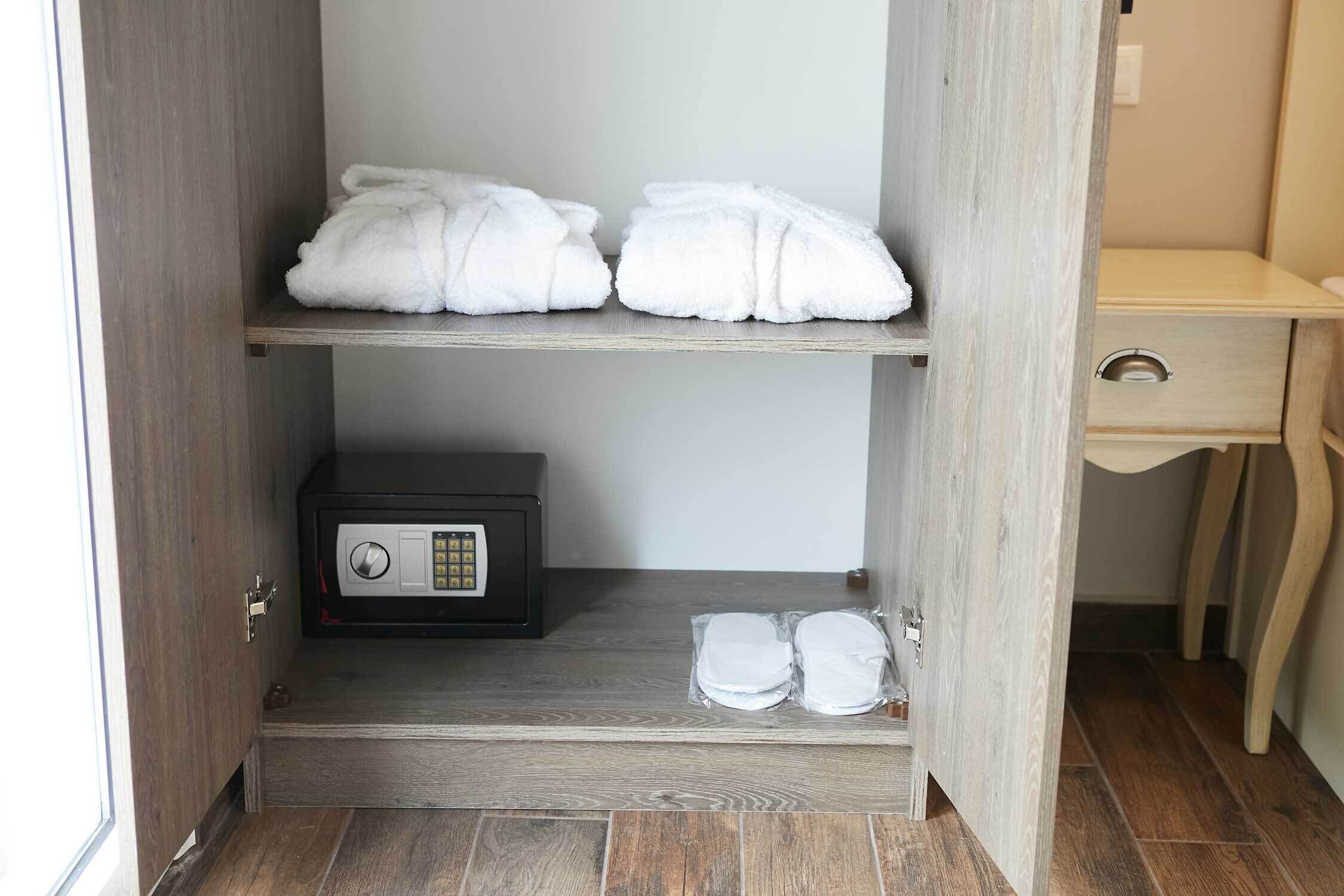 A hotel room with a wooden wardrobe containing towels and a safe.