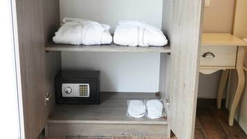A hotel room with a wooden wardrobe containing towels and a safe.