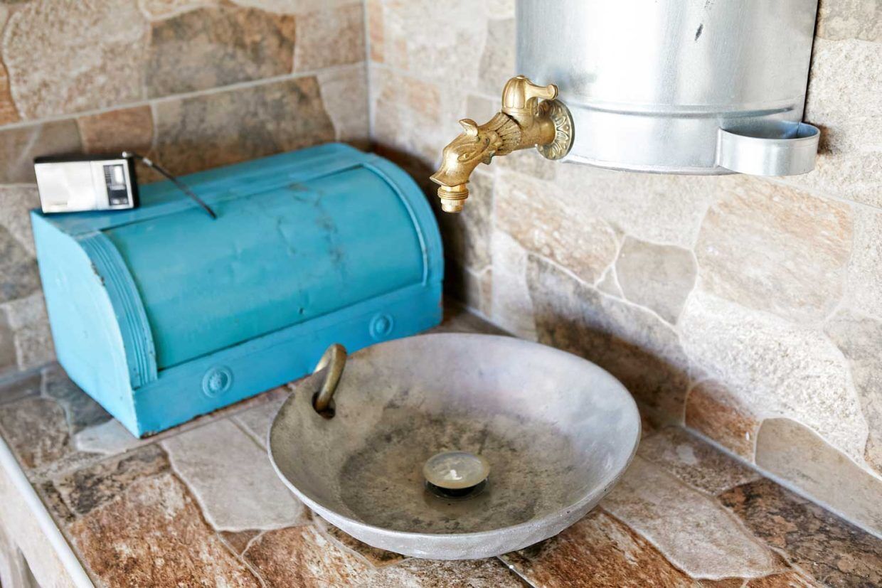 Een keuken met een achterwand van steen, een blauw apparaat, een metalen spoelbak en een kraan.