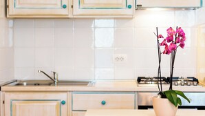 Een keuken met lichte houten kastjes, een witte betegelde achterwand, een gasfornuis en een roze vaas met orchideeën op het aanrecht.