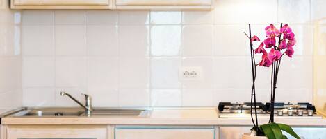A kitchen with light wooden cabinets, a white tiled backsplash, a gas stove, and a pink vase with orchids on the counter.