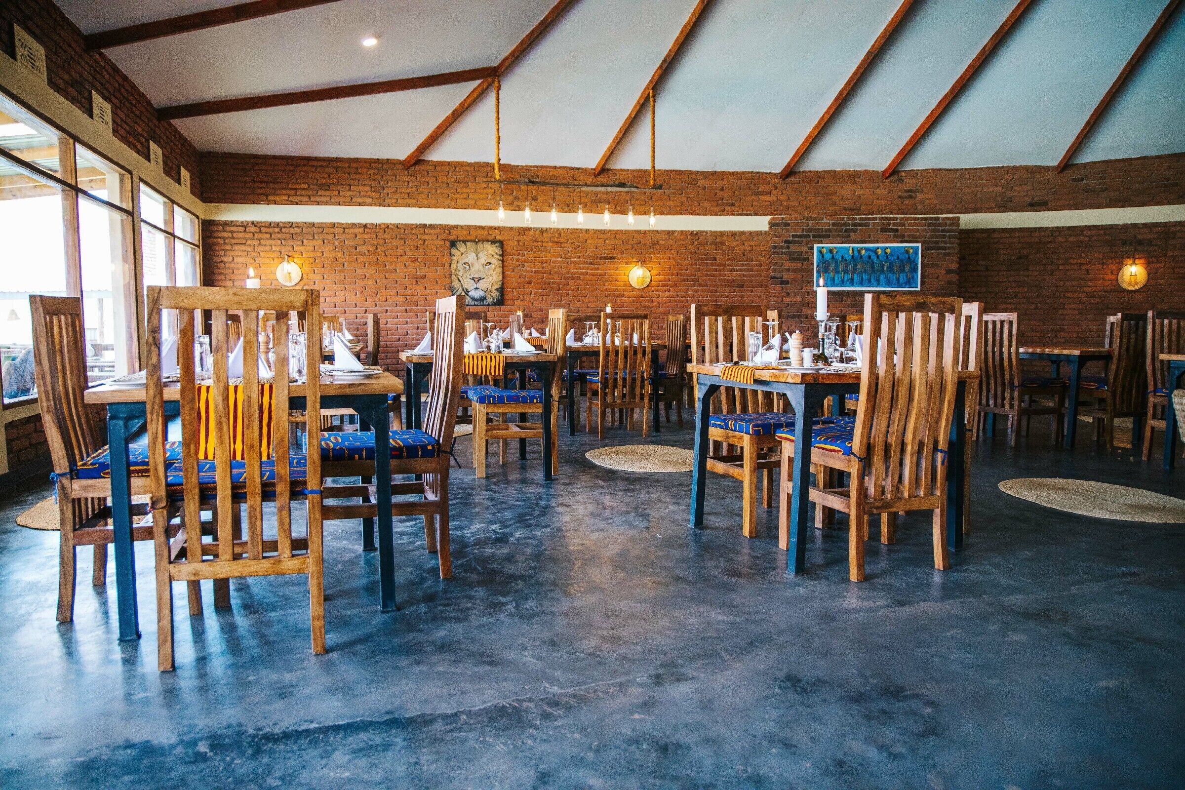 Un restaurante con sillas y mesas de madera, paredes de ladrillo y un techo alto con vigas a la vista.