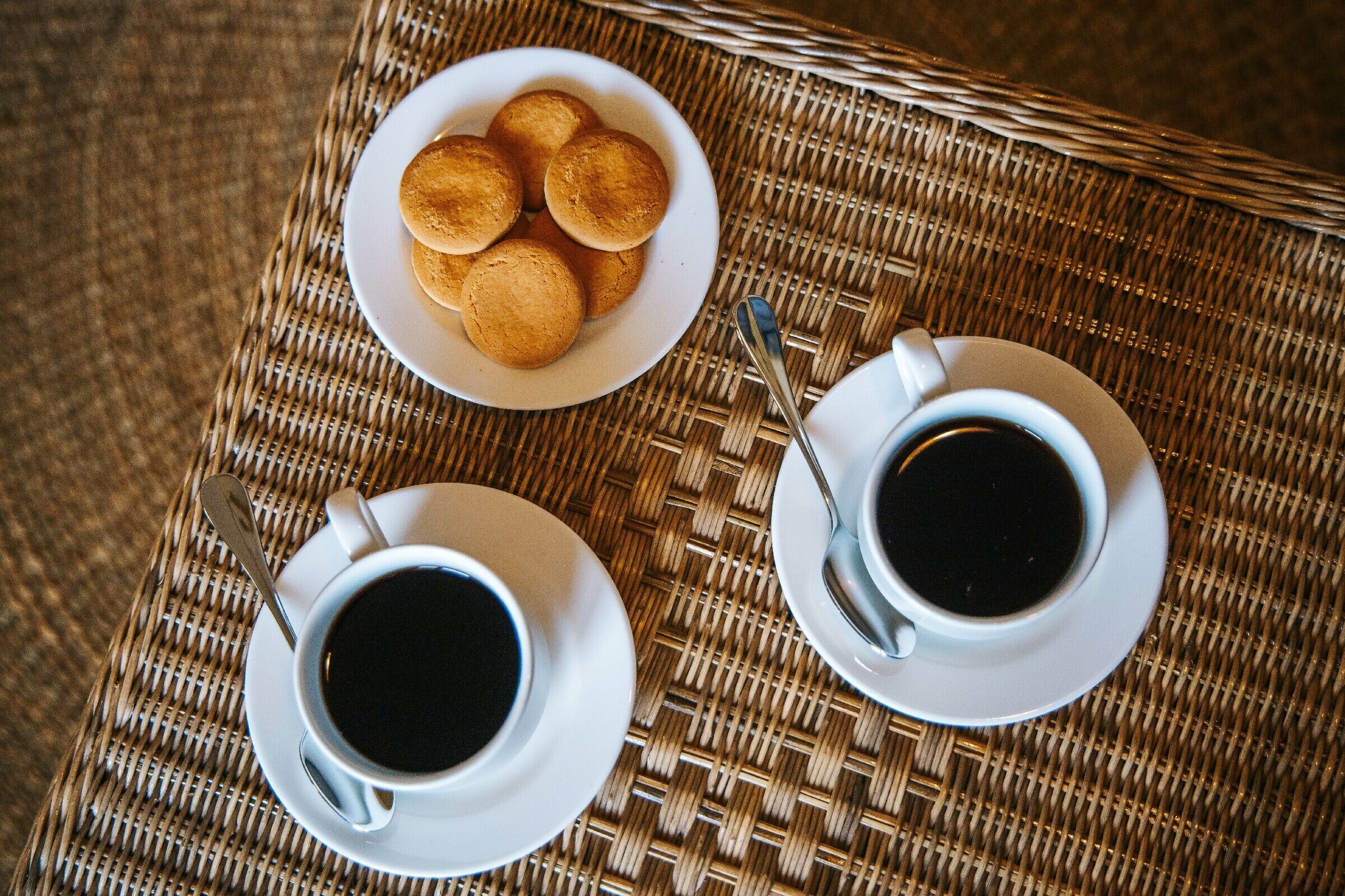 A wicker table with two white cups of coffee and a plate of pastries.