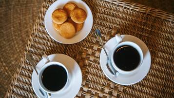 A wicker table with two white cups of coffee and a plate of pastries.