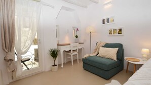 Een kamer met een groene bank, een wit bureau, een stoel, een klein tafeltje, een lamp en een potplant.