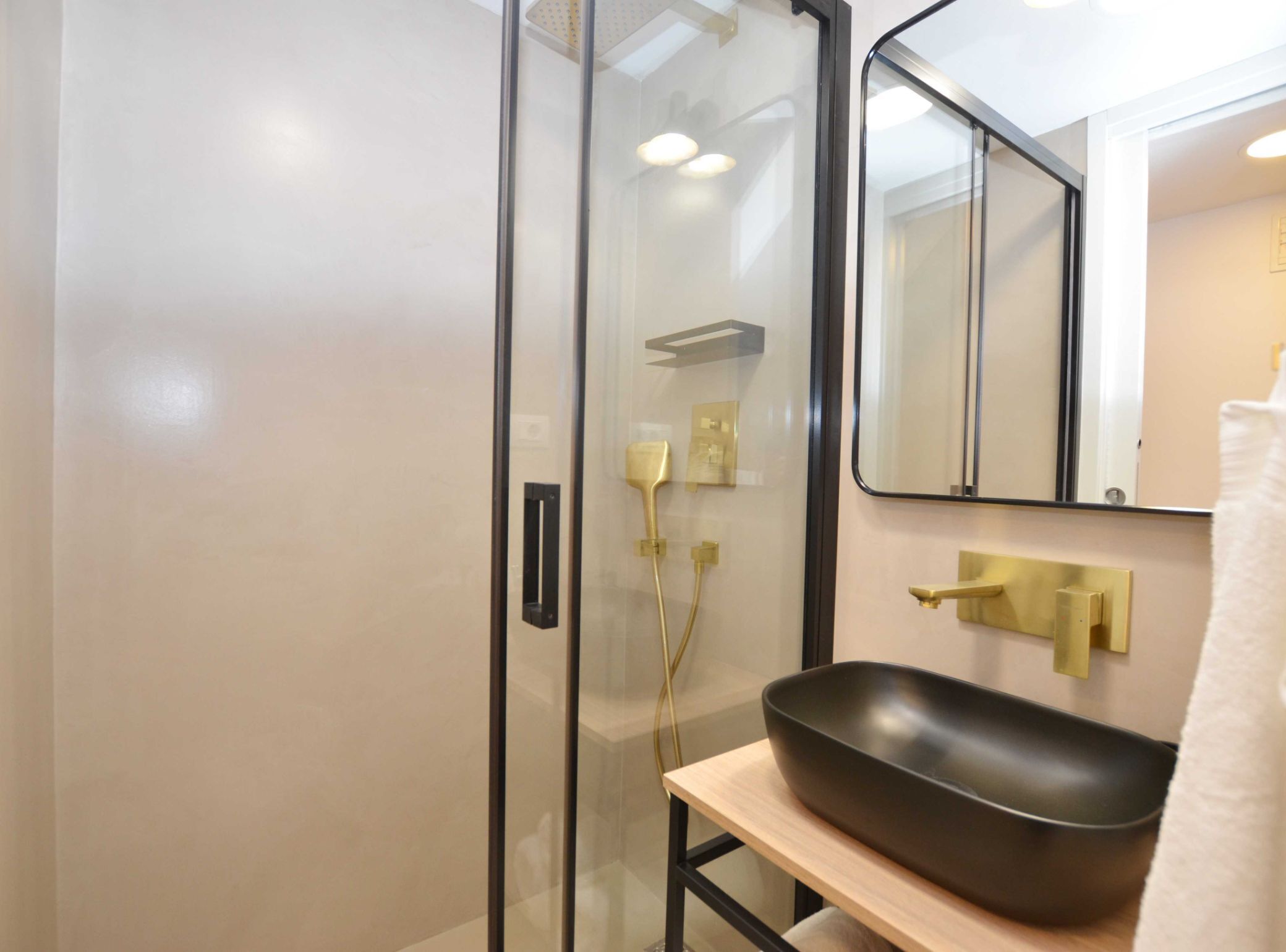 Une salle de bain moderne avec une douche à parois de verre, un lavabo noir et des accessoires dorés.