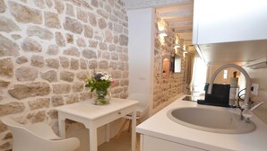Een kleine keuken met een stenen muur, een witte spoelbak, een witte tafel en een witte stoel.