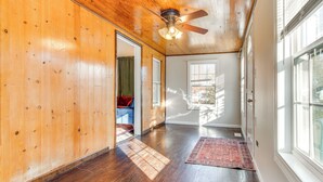 A hallway with wooden walls, a ceiling fan, and a view of a room with a window.
