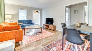 A living room with a sofa, TV, dining table, chairs, and a rug.