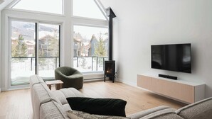 Ein modernes Wohnzimmer mit großem Fenster, Kamin, Flachbildfernseher und einer Couch.