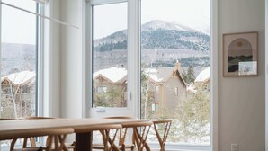 Ein Zimmer mit großen Fenstern und Blick auf einen verschneiten Berg sowie Wohnhäuser.