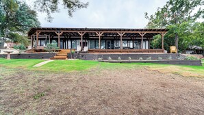 Ein hölzernes Pavillon mit überdachtem Sitzbereich, umgeben von einem angelegten Garten und Bäumen.