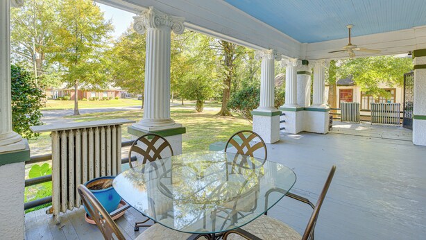 A covered outdoor patio with a glass table and chairs, white columns, and a view of the surrounding greenery. - 1 Mi to Dtwn Meridian: Historic Home w/ Porch! (Meridian)