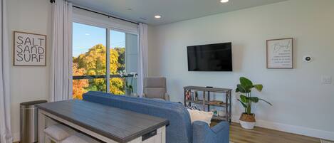 A modern living room with a blue sofa, a wooden dining table, and a TV mounted on the wall.