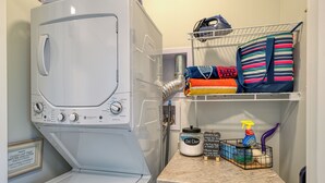 A laundry area with a front-loading washing machine, a shelf with folded towels, a laundry basket, and cleaning supplies.