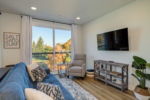 A modern living room with a large window, a sofa, a TV, and a small table with decorative items. - West Bay View: Penthouse Condo in Traverse City (Traverse City)