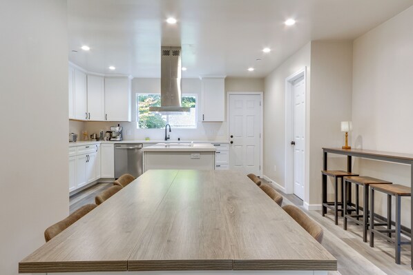 A modern kitchen with white cabinetry, a large wooden dining table, and a built-in oven.