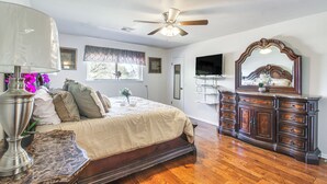 Un dormitorio con cama, cómoda, ventilador de techo y televisor en la pared.
