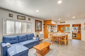 Una sala de estar con un sofá azul, una mesa de centro de madera y un comedor con una mesa y sillas de madera.