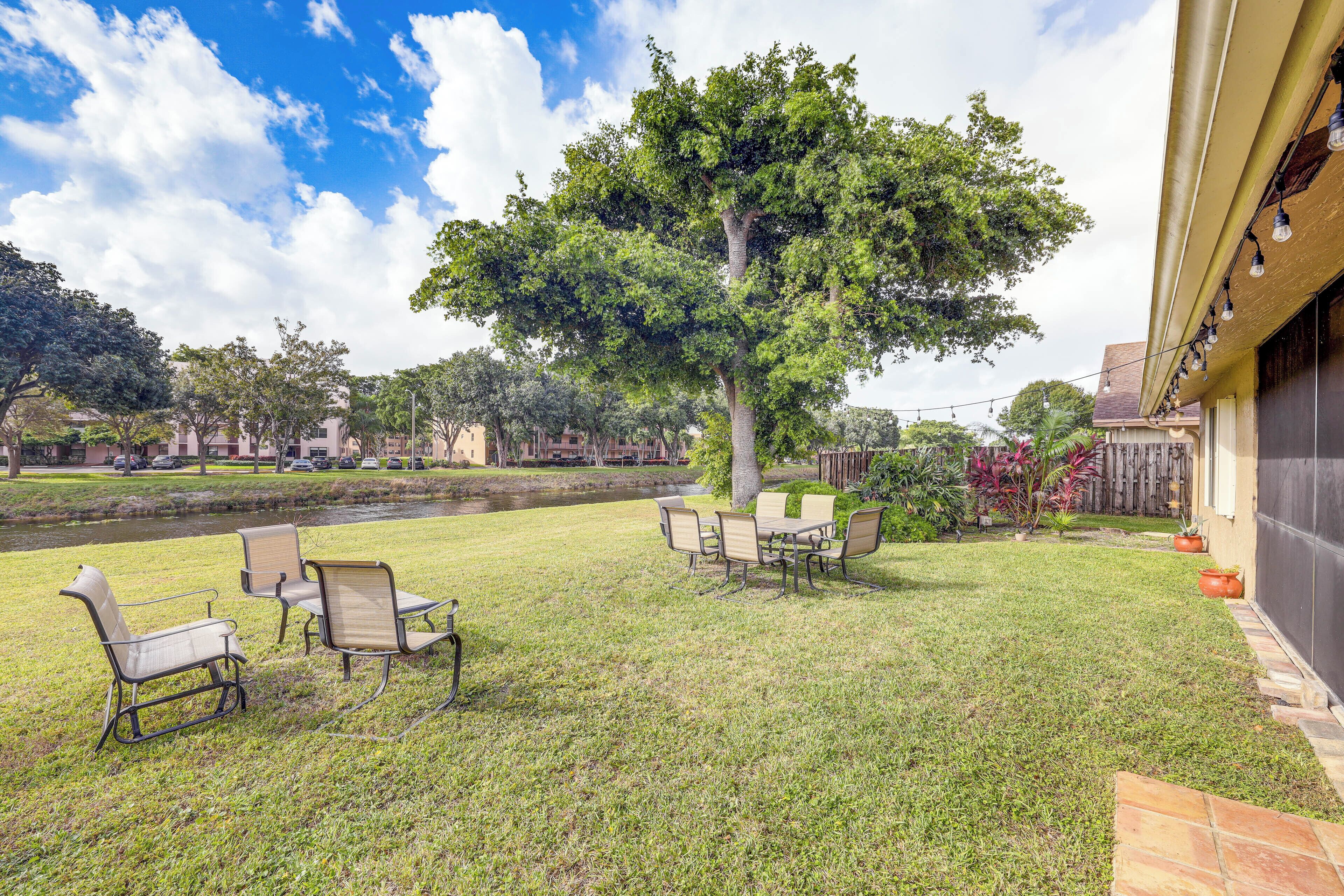 A grassy outdoor area with a dining table and chairs, a large tree, and a building with a garage.
