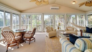 A sunroom with large windows, wicker chairs, a glass table, and a hammock. - Laid-back Luxury: Home w/ Pool Near Bowmans Beach (Sanibel)