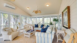A spacious sunroom with large windows, a ceiling fan, and a variety of seating options including a striped sofa, armchairs, and a hammock. - Laid-back Luxury: Home w/ Pool Near Bowmans Beach (Sanibel)