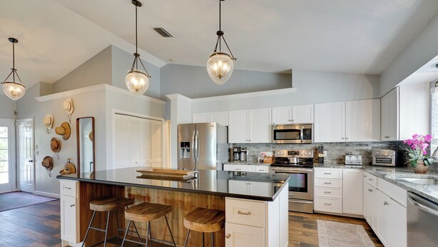 A modern kitchen with white cabinets, stainless steel appliances, and a central island with stools. - Laid-back Luxury: Home w/ Pool Near Bowmans Beach (Sanibel)