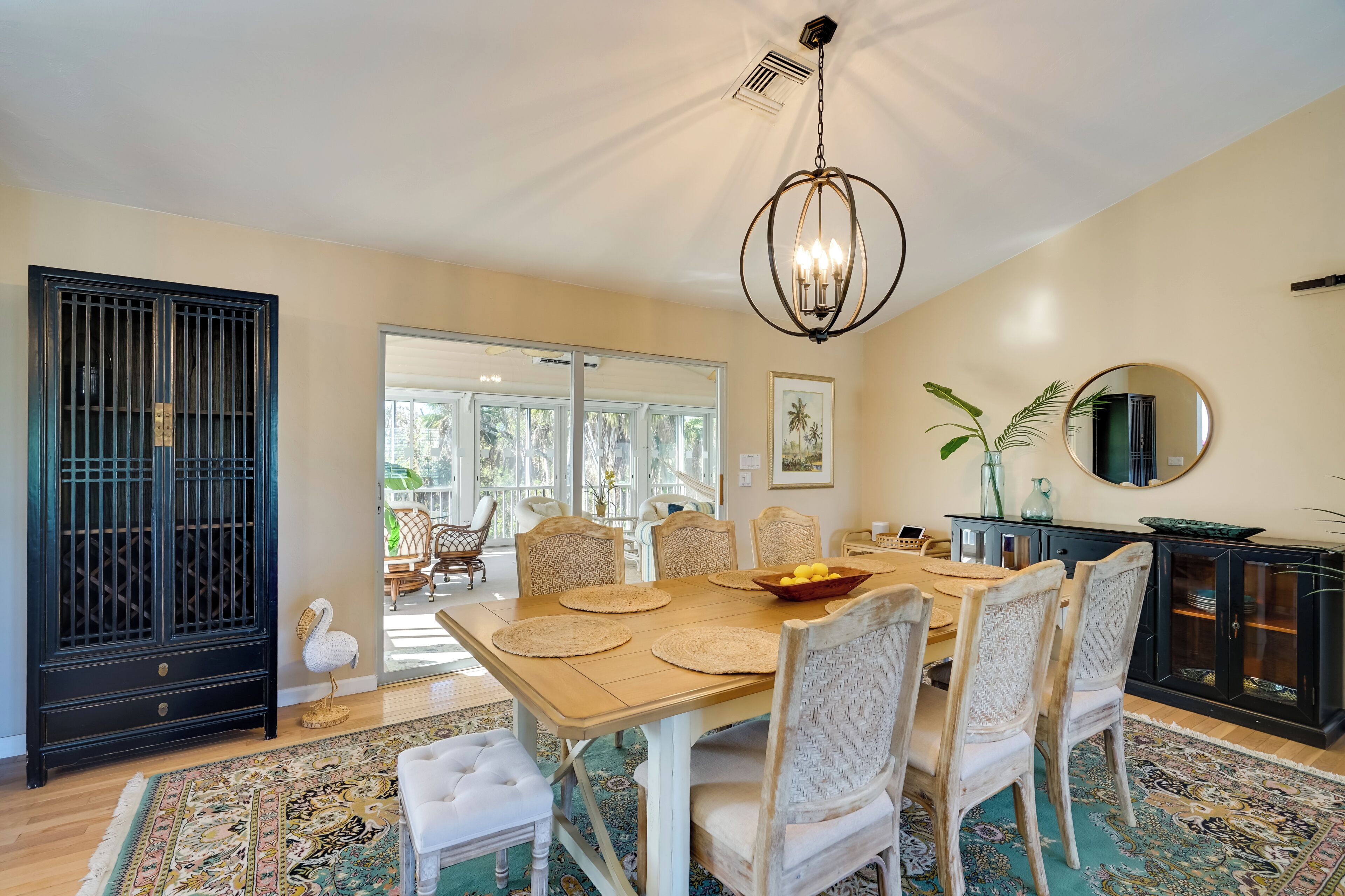 A dining area with a wooden table, white upholstered chairs, a black cabinet, and a chandelier.