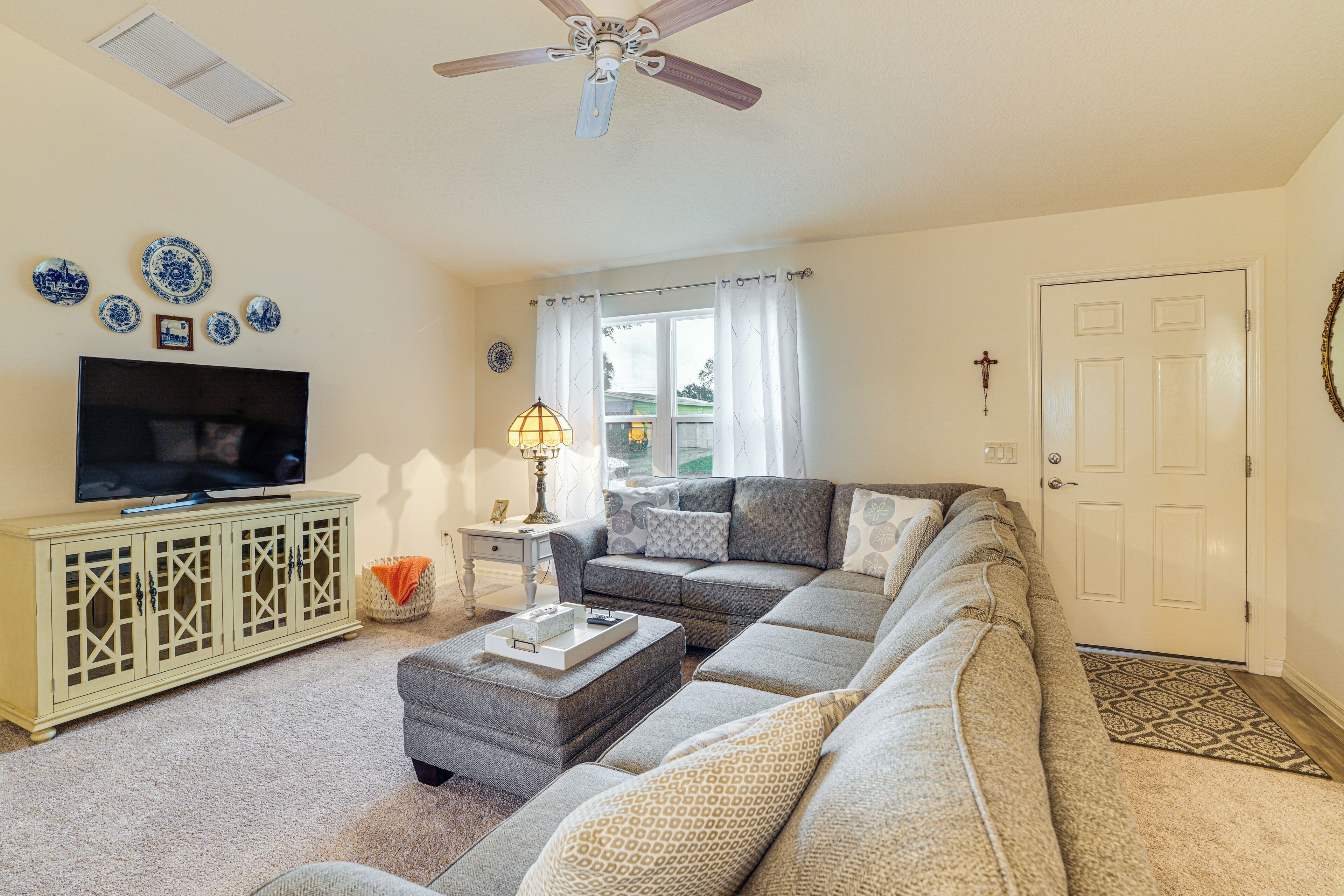 A living room with a sofa, ottoman, TV, and decorative plates on the wall.