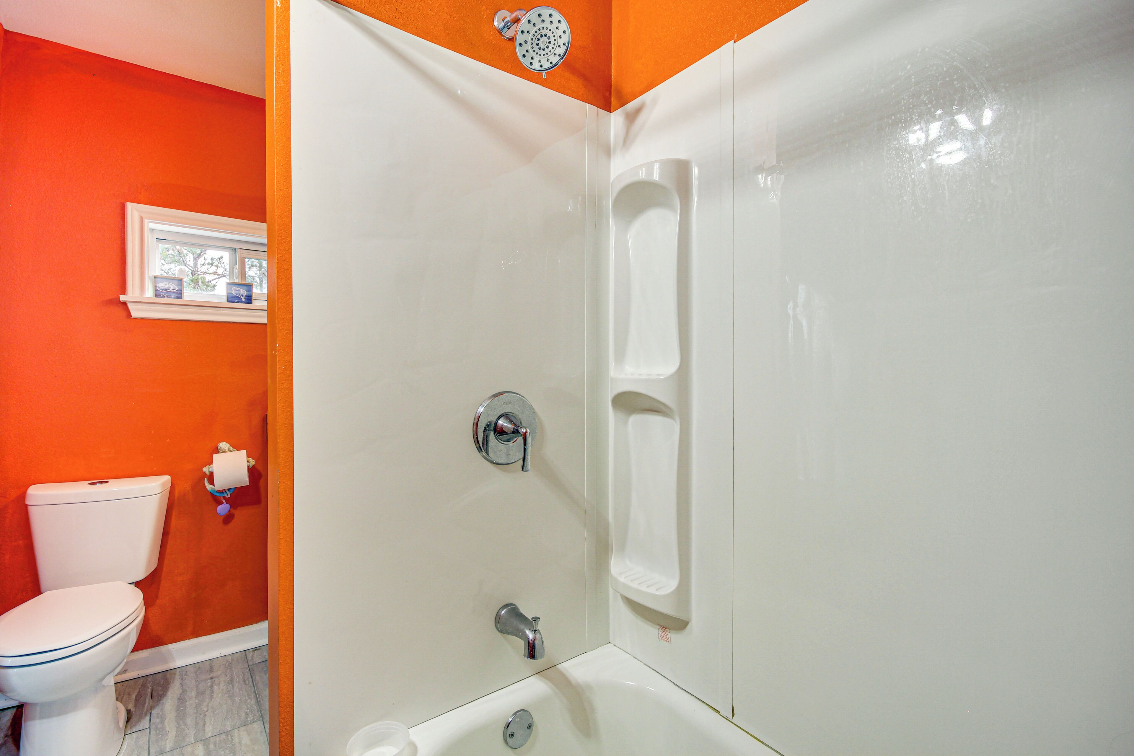 A bathroom with a white bathtub, a white toilet, and an orange wall.