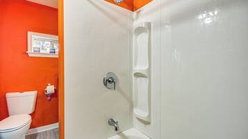 A bathroom with a white bathtub, a white toilet, and an orange wall.