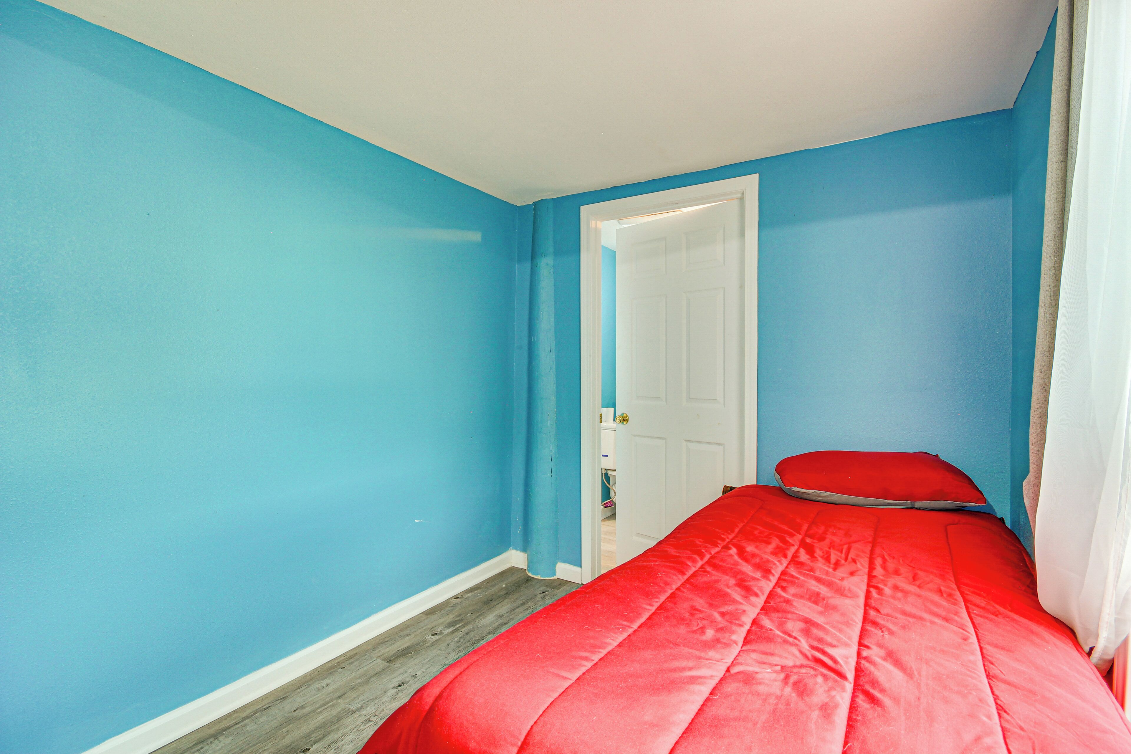A bedroom with blue walls, a wooden floor, a white door, and a red bed.